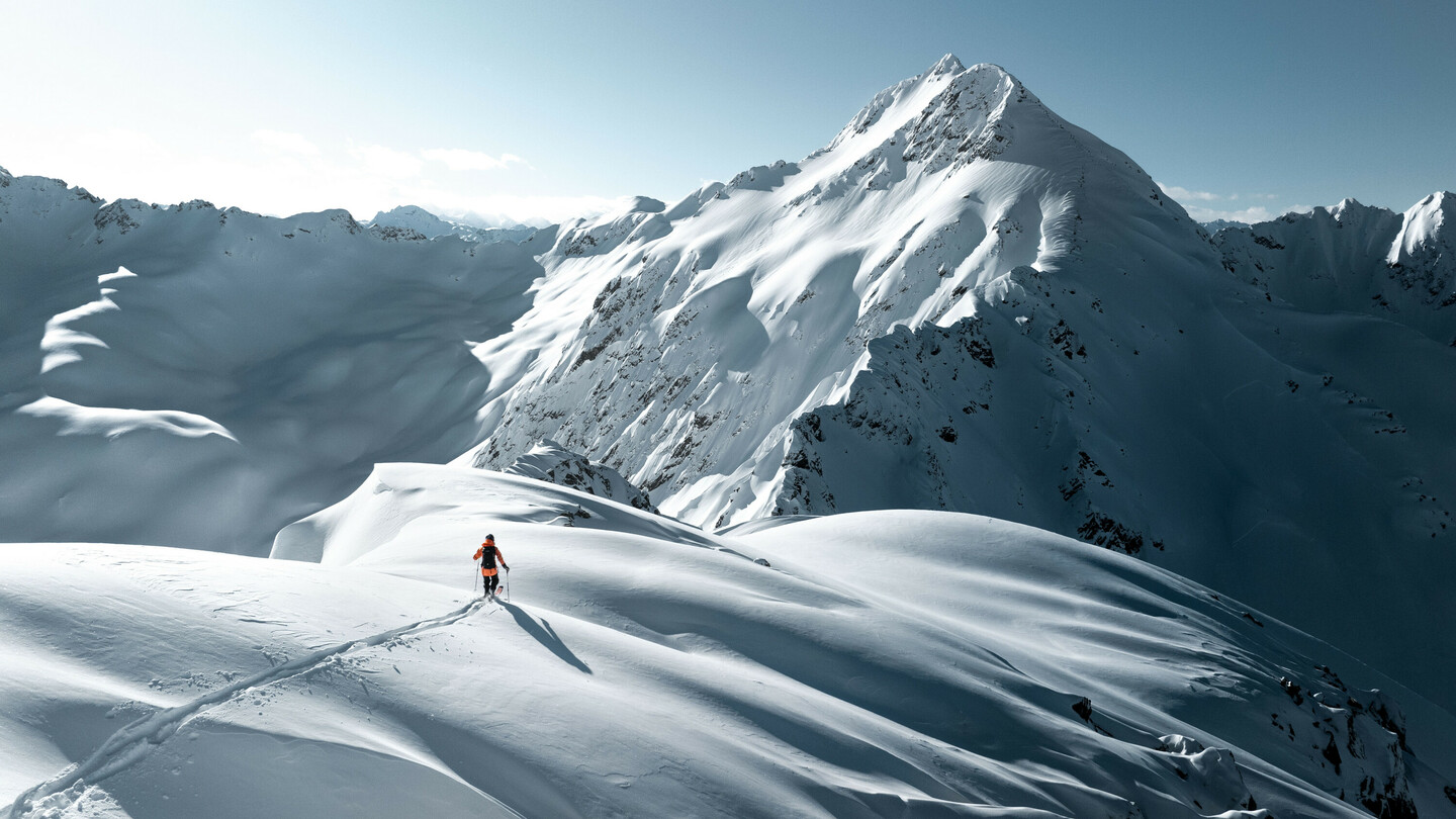 Un skieur sur un paysage de montagne enneigé sous un soleil éclatant, entouré de sommets majestueux et de neige vierge.